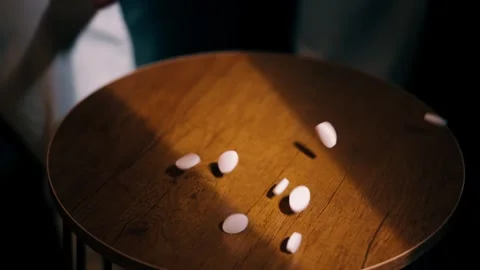 White round tablets scattered across a wooden table as a hand sets them down in Stock Footage 343803839