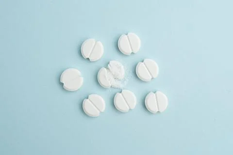 White round tablets scattered on a light blue background, one pill broken w.. Stock Photos