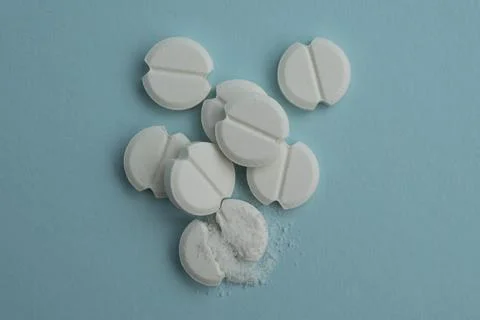 White round tablets scattered on a light blue background, one pill broken w.. 库存照片