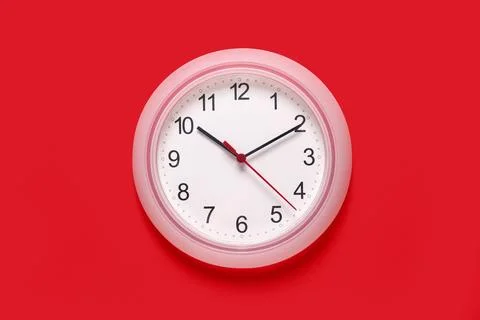 White round wall clock with black numbers and red second hand on a bright red Stock Photos