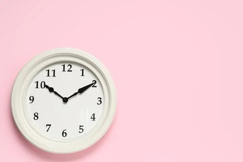White round wall clock with black numbers and hands on a pastel pink backgrou Stock Photos
