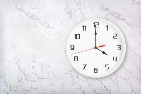 White round wall clock on white natural marble background. Four o'clock Stock Photos