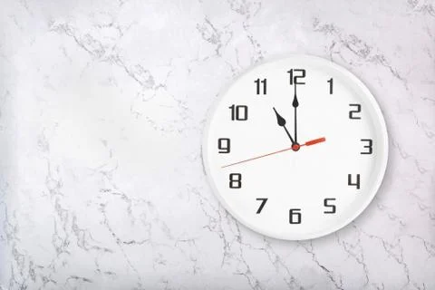 White round wall clock on white natural marble background. Eleven o'clock Stock Photos