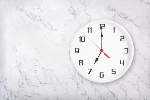 White round wall clock on white natural marble background. Seven o'clock Stock Photos