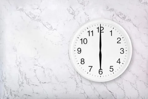 White round wall clock on white natural marble background. Six o'clock. Stock Photos