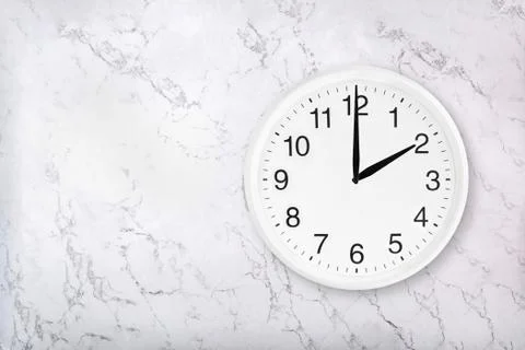 White round wall clock on white natural marble background. Two o'clock. Stock Photos