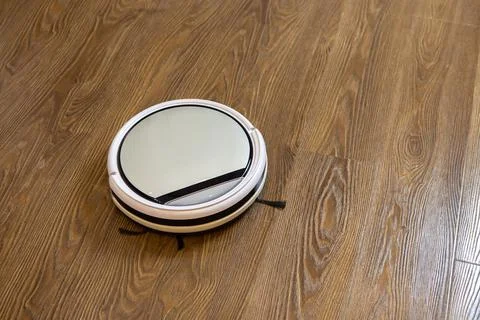 White round wireless robot vacuum cleaner on brown laminate floor. Concept ev Stock Photos