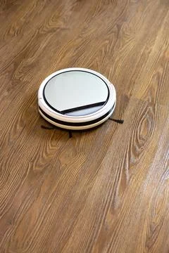 White round wireless robot vacuum cleaner on brown laminate floor. Concept ev Stock Photos