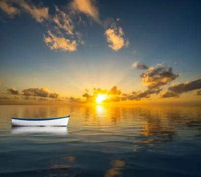 White rowing boat adrift on open ocean and drifting towards the sunset Stock Photos