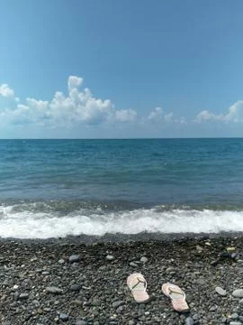 White rubber flip-flops lie on the beach in the direction of the sea Stock Photos
