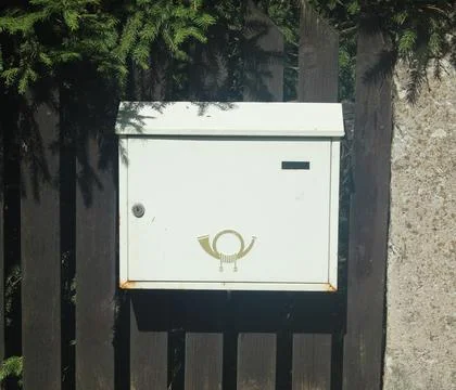 White Rustic Metal Mailbox Attached to Dark Wooden Fence with Postal Horn Emblem Stock Photos