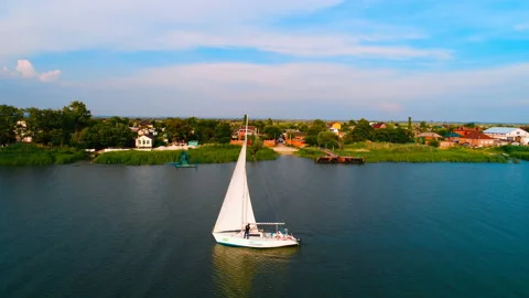 White sailing boat floating on the river near a small village. Copter ( drone )  Stock Footage 119513724