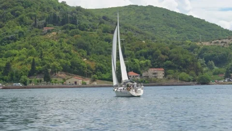 A white sailing boat sails on a blue sea against a background of green mountains Stock Footage 210853409