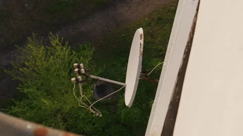 White Satellite Dish Installed on Building Facade with View of Trees Below Vídeo Stock 334132449