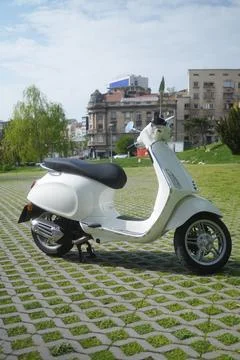White scooter parked on paved surface with city buildings in background Stock-Fotos