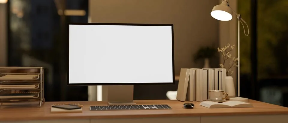 White screen computer with books and aside lamp on wooden table in a dim li.. Illustrazione stock