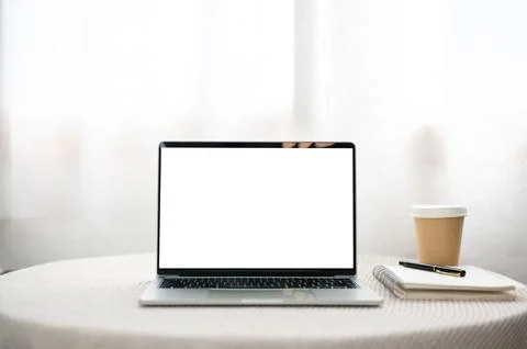 White screen laptop aside notebook with pen and coffee cup on round table i.. Illustrazione stock