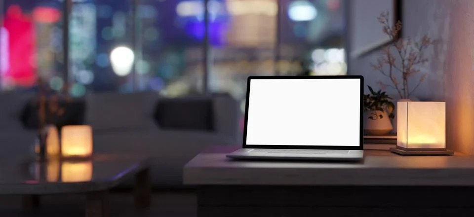 A white-screen laptop computer and a table lamp on a table in a modern, dar.. Illustrazione stock