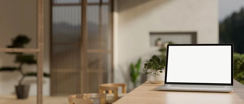 A white-screen laptop computer mockup on a wooden dining table in a cosy, S.. Illustrazione stock