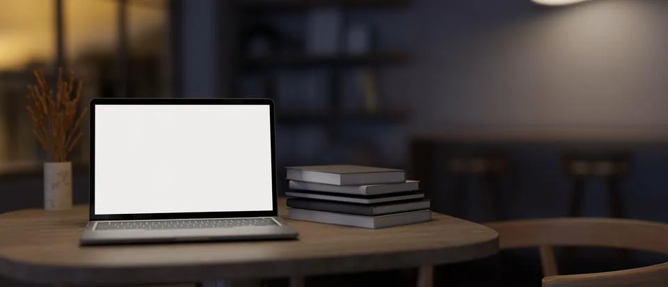 A white-screen laptop computer mockup and books on a table in a modern dark.. Illustrazione stock