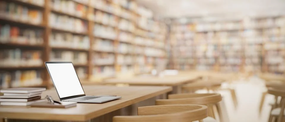 A white-screen laptop computer mockup and books on a wooden table in a spac.. Illustrazione stock