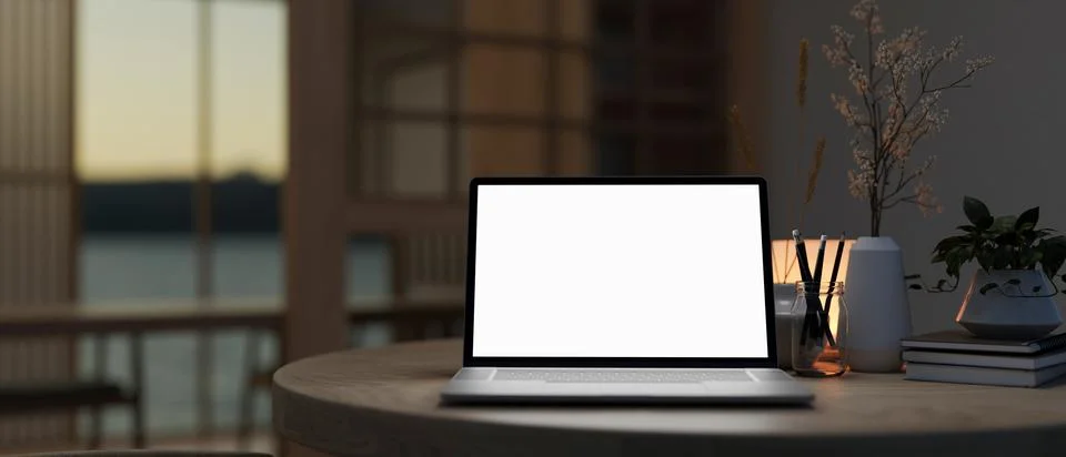 A white-screen laptop computer on a table in a modern dark room. Illustrazione stock
