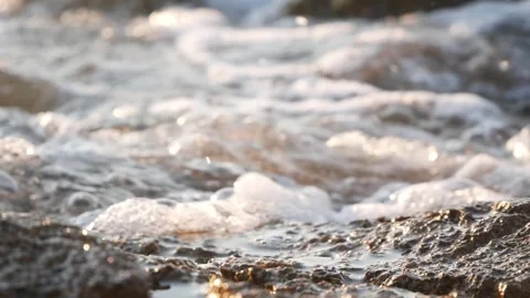 White sea foam and bubbles washing over dark wet rocks Stock Footage 337418640