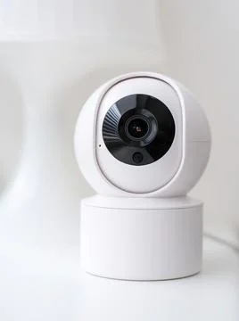 A white security camera with a black lens is mounted on a white surface. The Stock Photos