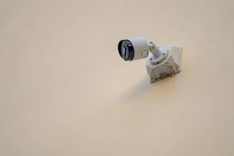 White security camera mounted on beige wall Stock Photos