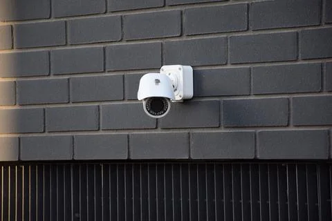 White security CCTV camera mounted on a dark brick wall of a building Stock Photos