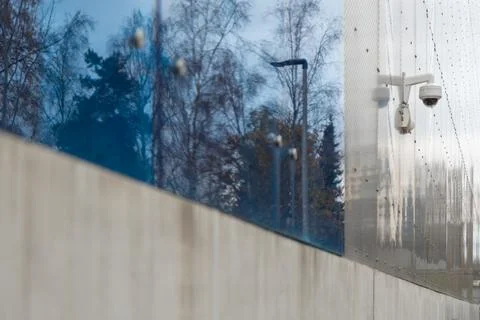 A white security dome camera is mounted on a grey perforated metal wall with  Stock Photos