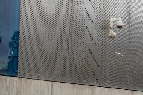 A white security dome camera is mounted on a grey perforated metal wall with  Stock Photos