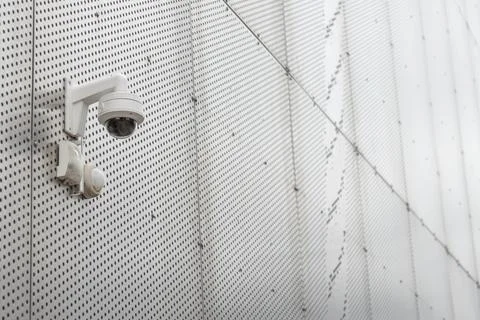 A white security dome camera is mounted on a grey perforated metal wall with  Stock Photos