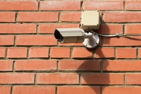 White security surveillance camera on the old red brick wall of a house. Conc Stock Photos