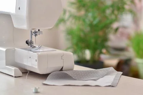 A white sewing machine stands on the table next to the fabric. Atelier and Stock Photos