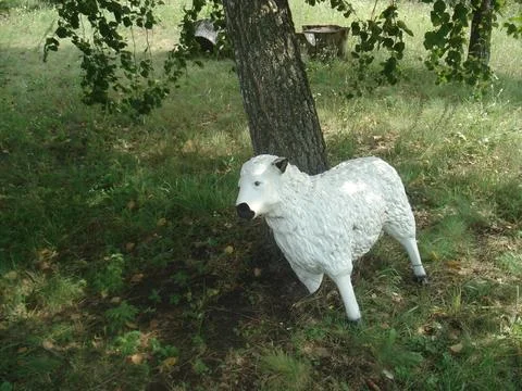 White Sheep Statue Under a Tree in a Green Meadow Stockfoto's