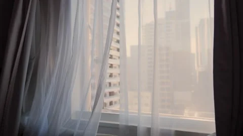 White sheer curtains gently swaying in the breeze revealing a modern city view 스톡 동영상 344010794