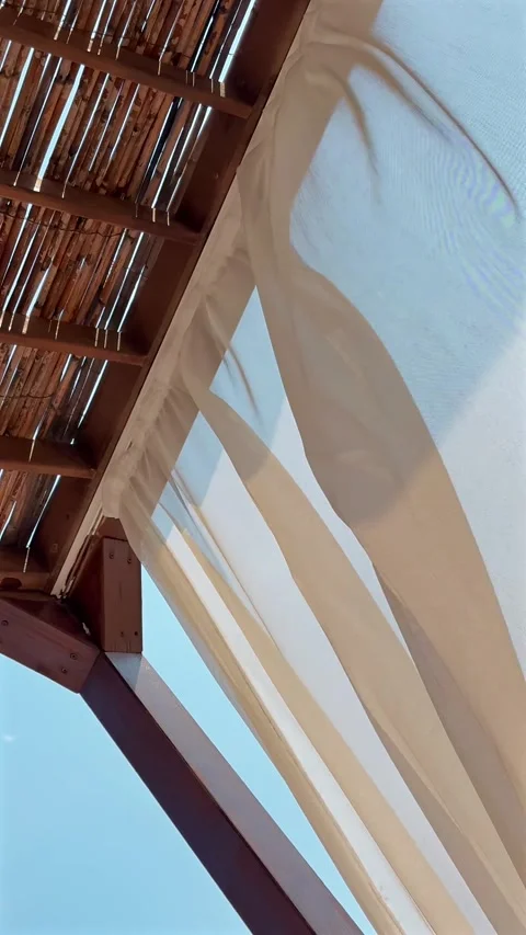 White sheer curtains moving gently beneath a wooden pergola against Stock Footage 345642354