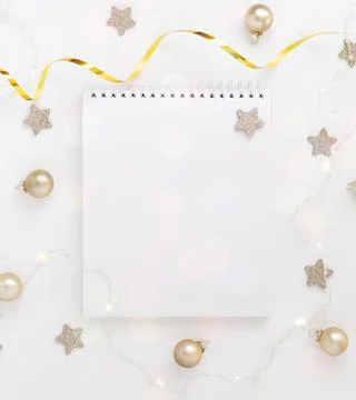 White sheet of notebook on white table with stars, Christmas balls and festive Stock Photos
