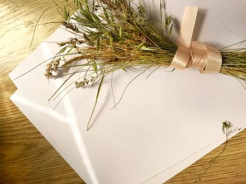 White sheet of paper and a bundle of meadow grass with ribbon on a wooden tab Stock Photos
