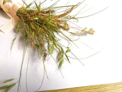 White sheet of paper and a bundle of meadow grass with ribbon on a wooden tab Stock Photos