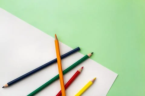 White sheet of paper and five pencils on a pea green color paper background.  Stock Photos