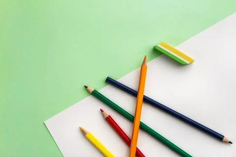 White sheet of paper, five pencils and an eraser on a light green paper backg Stock Photos