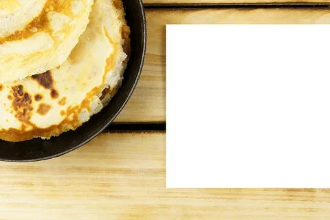 White sheet of paper next to a stack of pancakes on a wooden background. Stock Photos