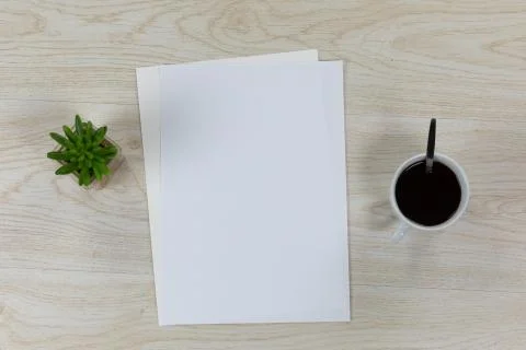 White sheet of papers surrounded by a plant and coffee on wood table Stock Photos