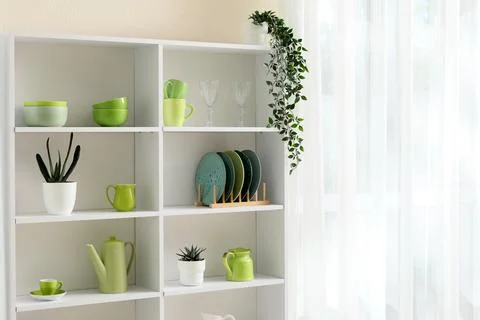 White shelving unit with green kitchenware and potted plants next to a sheer  Stock Photos