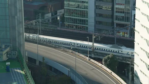 White shinkansen bullet train passing by urban rooftops and sports court. 스톡 동영상 333949055