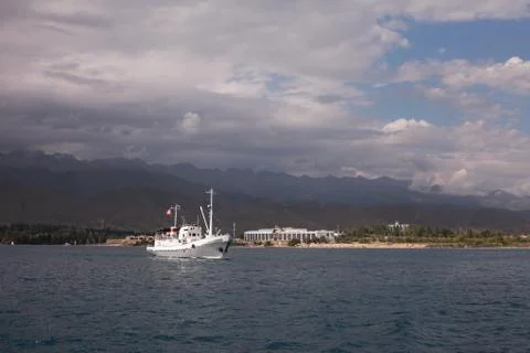 The white ship departs from the coast. Mountains of Kyrgyzstan. Bluewater. Stock Photos