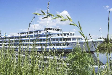 A white ship sails along the river on a clear summer day. Stock Photos