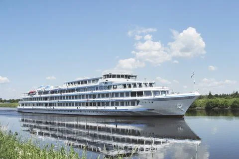 A white ship sails along the river on a clear summer day. Stock Photos